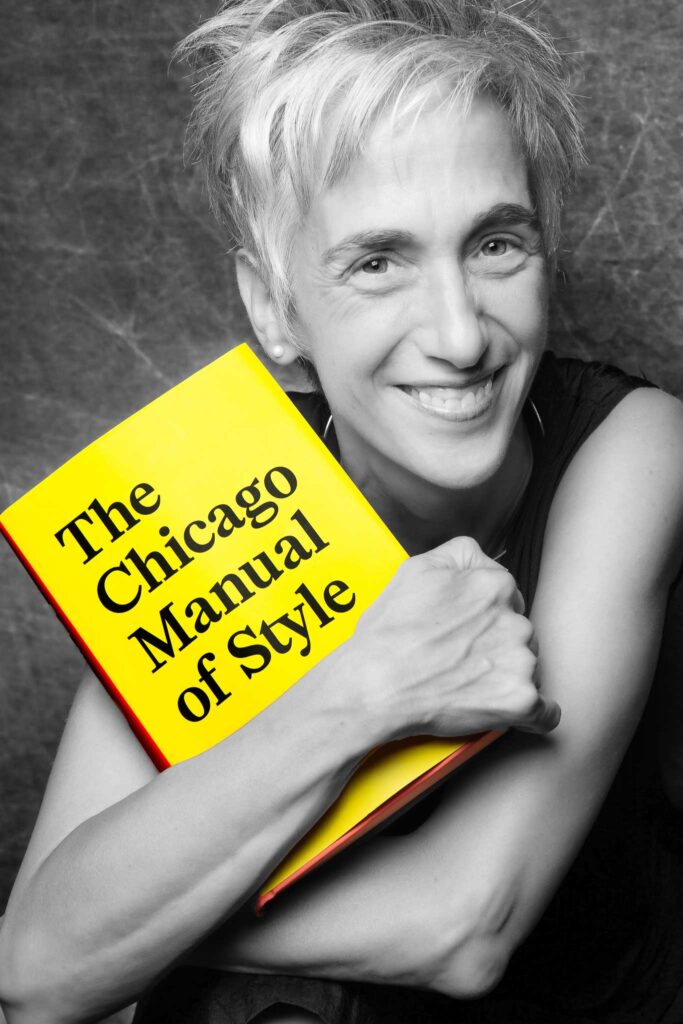 Black and white headshot of a smiling woman with a silver pixie haircut hugging a copy of the Chicago Manual of Style, which appears in its full color yellow cover with black typeface